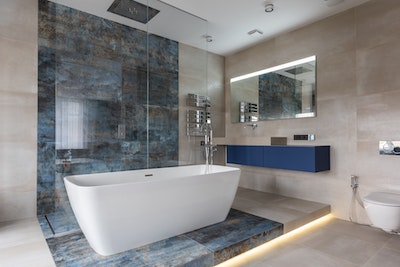 modernes Badezimmer mit großformatigen Fliesen in beige und blau marmoriert und mit einer im Raum stehender Badewanne